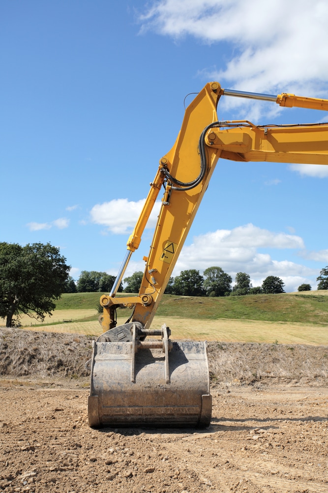 Bras et godet d'une excavatrice jaune sur un chantier de terrassement sous un ciel bleu dégagé.